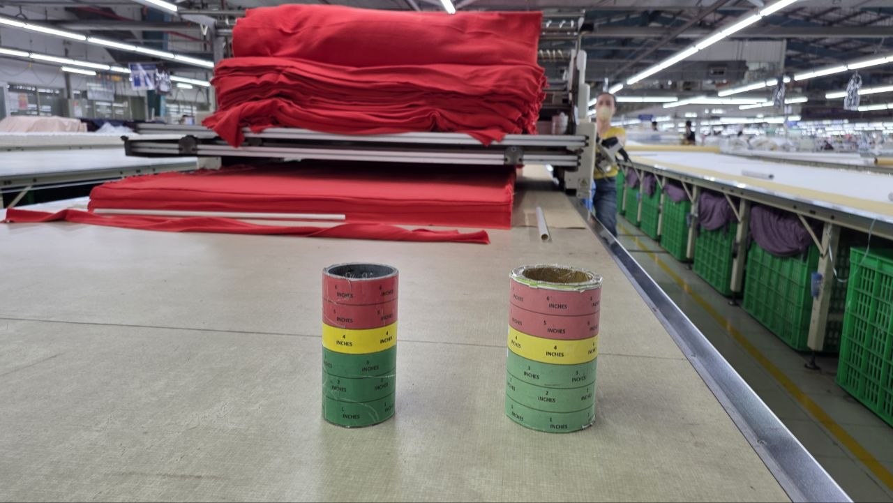 Actual garment cutting table with red fabric lay and two color-coded inch height gauges