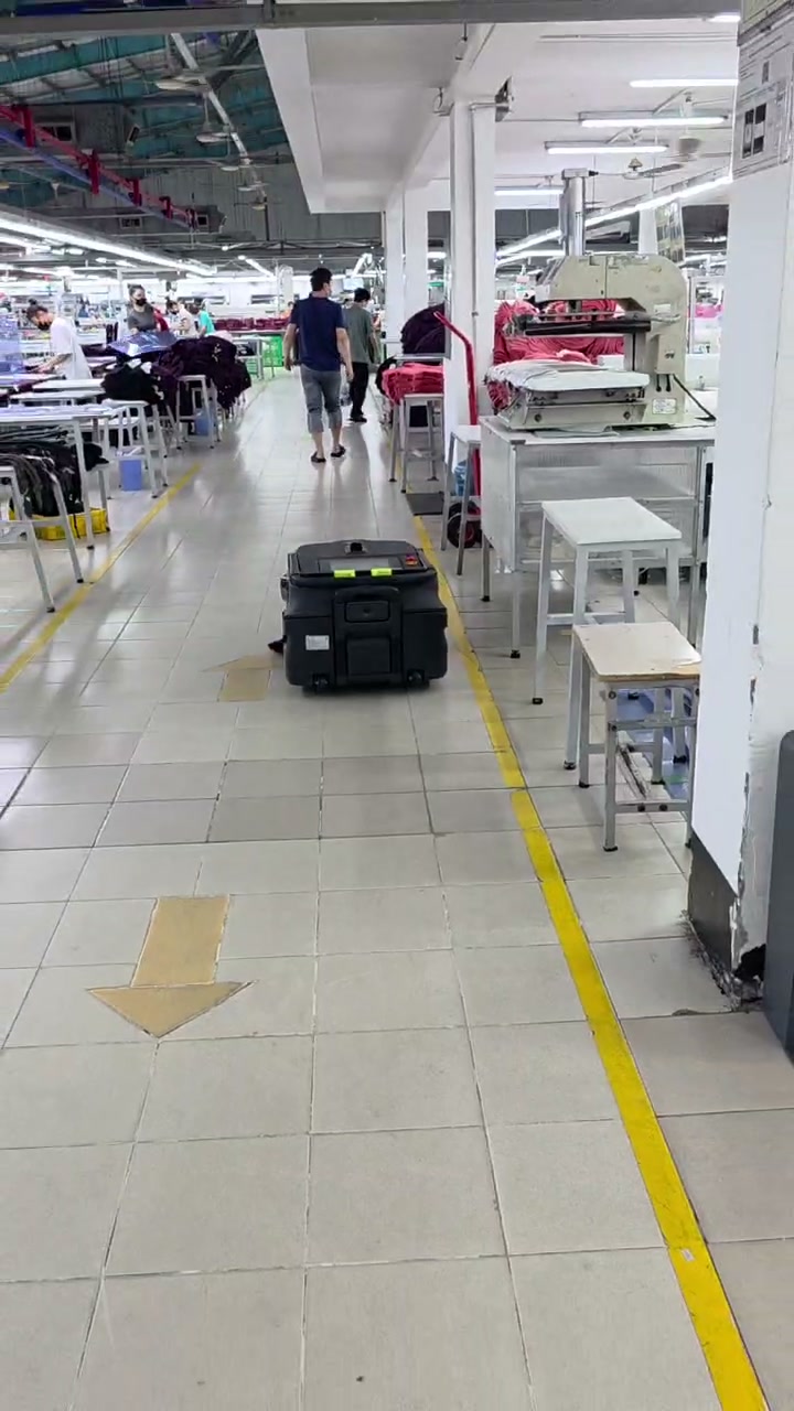 Still frame from garment factory cleaning robot route video showing robot movement along a marked sewing-floor aisle